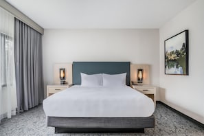 A hotel room with a large bed, two bedside tables with lamps, a painting on the wall, and a window with curtains. - DoubleTree Suites by Hilton Raleigh - Durham (Durham)