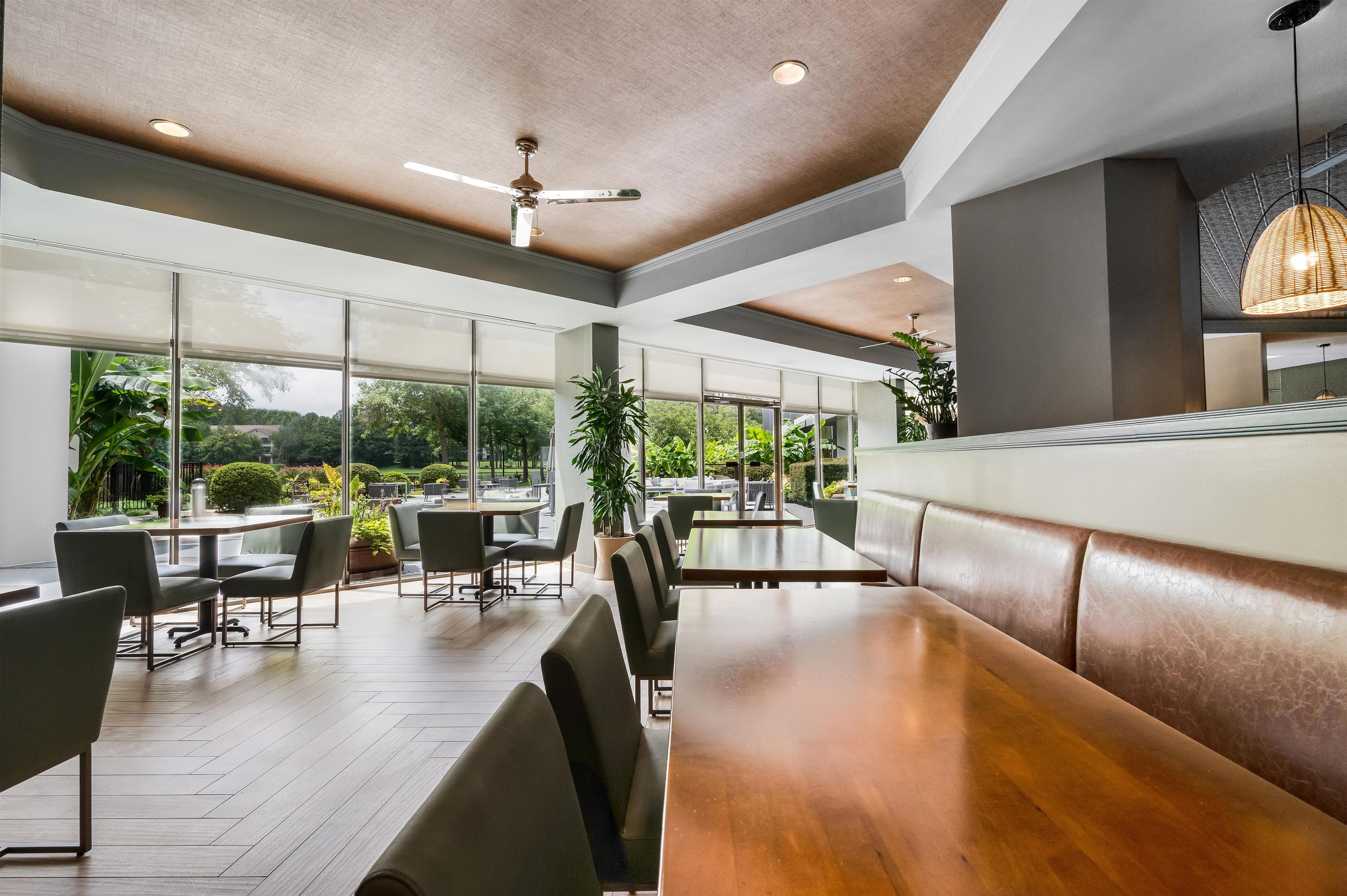 A modern dining area with large windows, wooden tables, and chairs.