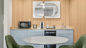Une cuisine moderne équipée d’un four à micro-ondes, d’une machine à café et d’un lave-vaisselle. On y trouve une table ronde devant laquelle sont placées deux chaises vertes.