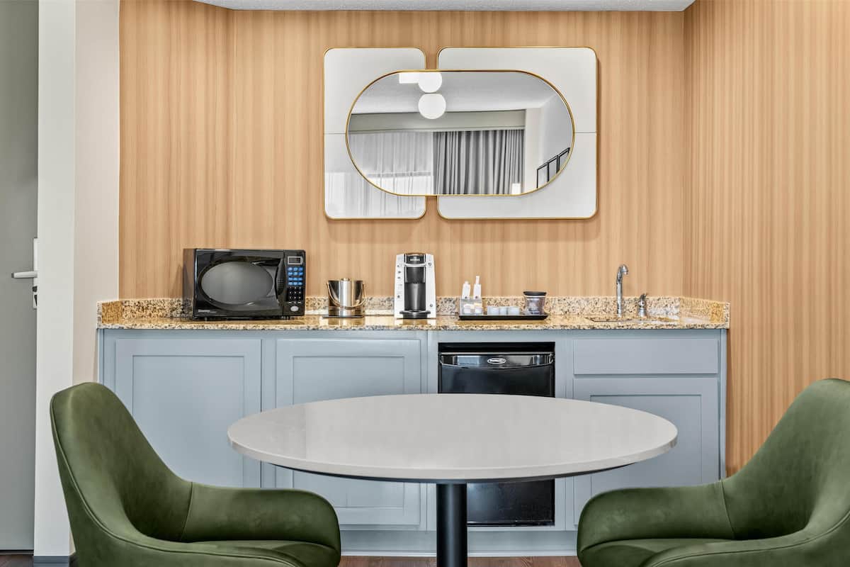 A modern kitchen with a microwave, coffee maker, and dishwasher. There is a round table with two green chairs in front.