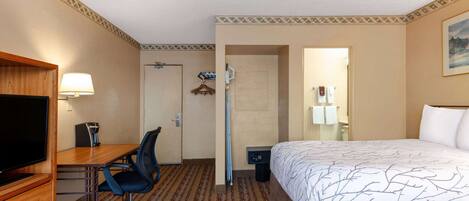 A hotel room with a bed, a desk with a chair, a television, and a lamp.