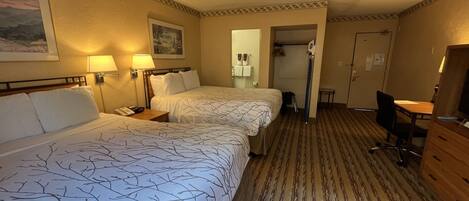 A hotel room with two beds, a desk, a chair, a lamp, and a mirror.