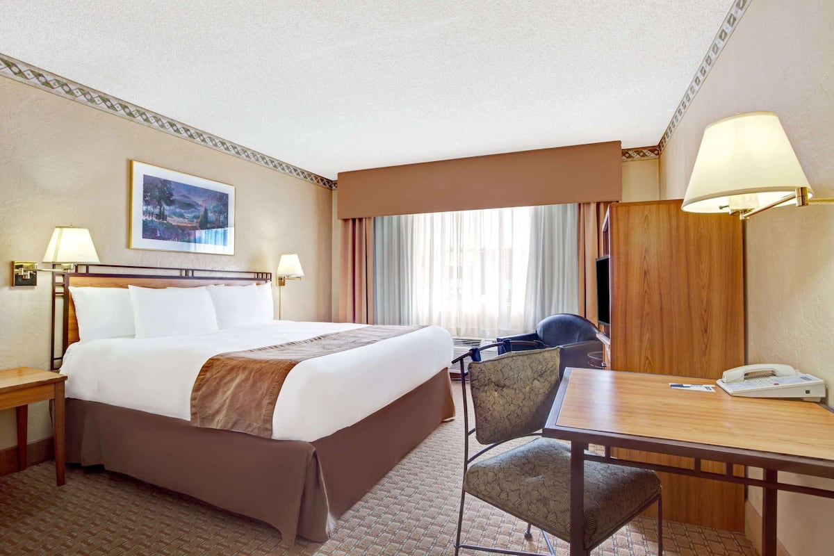 Quarto de hotel com uma cama grande, uma mesa com telefone e uma cadeira.