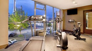 A gym with a treadmill, stationary bike, and exercise equipment. It has large windows with a view of the Space Needle. - Travelodge by Wyndham Seattle By The Space Needle (Seattle)