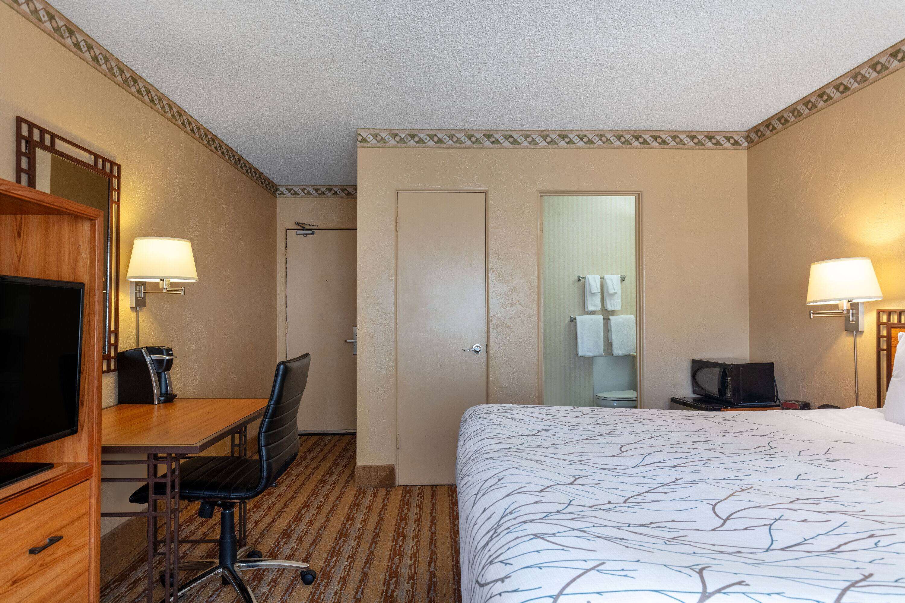 Una camera d'albergo con un letto, una scrivania, una sedia, una televisione e un bagno visibile attraverso una porta.
