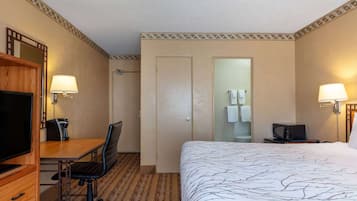 Una camera d'albergo con un letto, una scrivania, una sedia, una televisione e un bagno visibile attraverso una porta.
