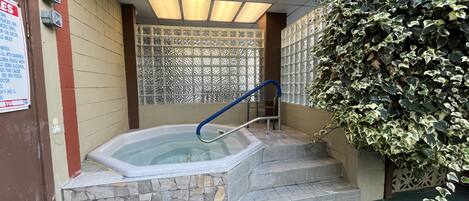 A hot tub with stone steps, a blue handrail, and a privacy screen.