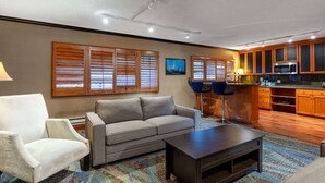A living room with a sofa, armchair, and coffee table, a kitchen area with wooden cabinets and a microwave, and a window with blinds. - Travelodge by Wyndham Seattle By The Space Needle (Seattle)