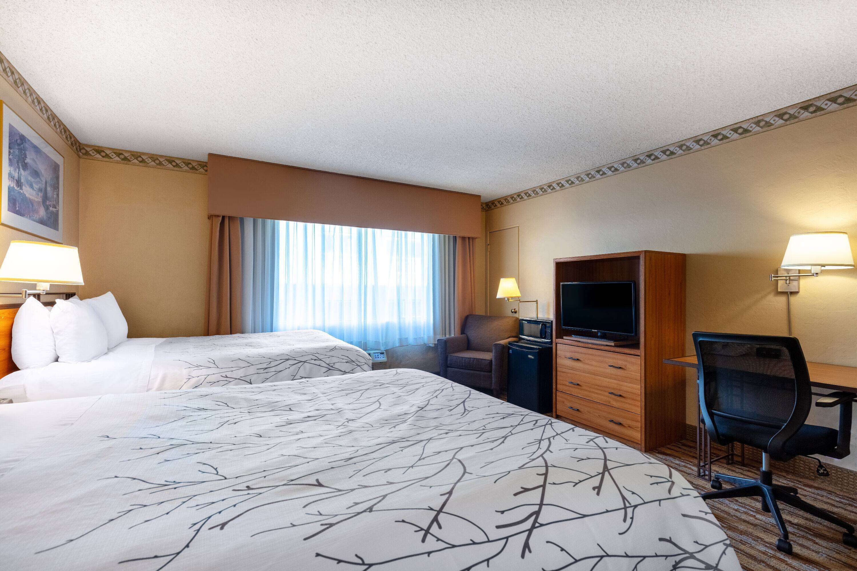 A hotel room with two beds, a desk, a chair, a TV, and a dresser.