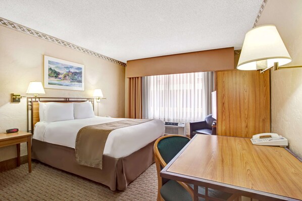 A hotel room with a bed, bedside tables, a desk, a chair, a lamp, a phone, and a painting on the wall.