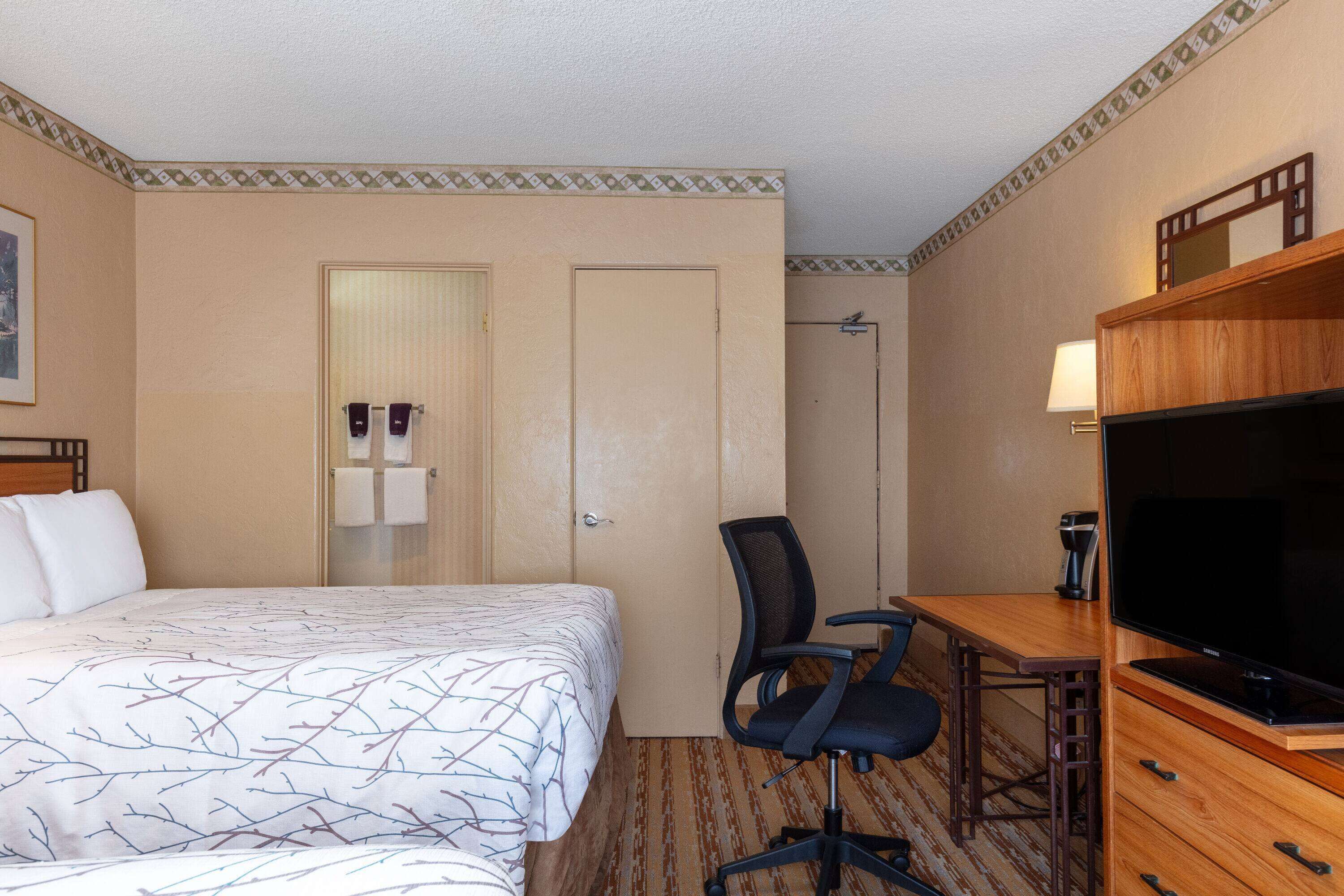 A hotel room with a bed, a desk with a chair, a television, and a wardrobe.