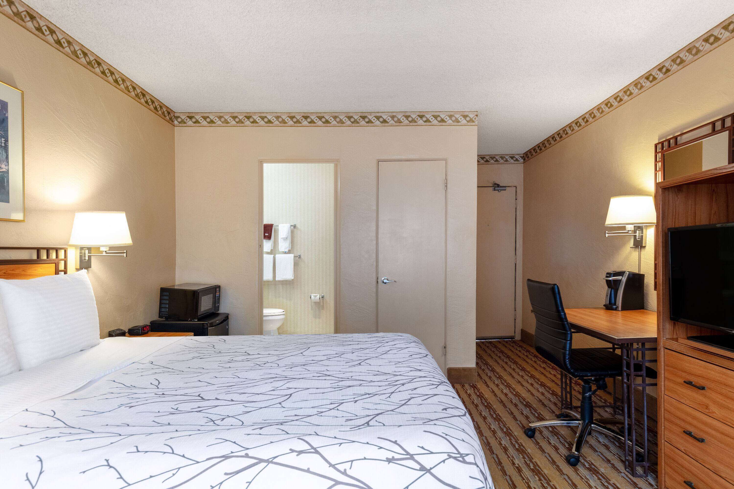 A hotel room with a large bed, a desk with a chair, a television, and a bathroom with a toilet and towel rack.