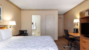 A hotel room with a large bed, a desk with a chair, a television, and a bathroom with a toilet and towel rack.