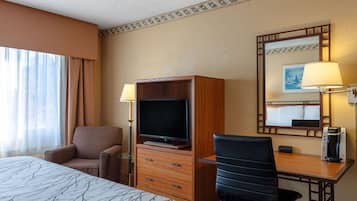A hotel room with a bed, a TV, a desk, a chair, a coffee maker, and a lamp.