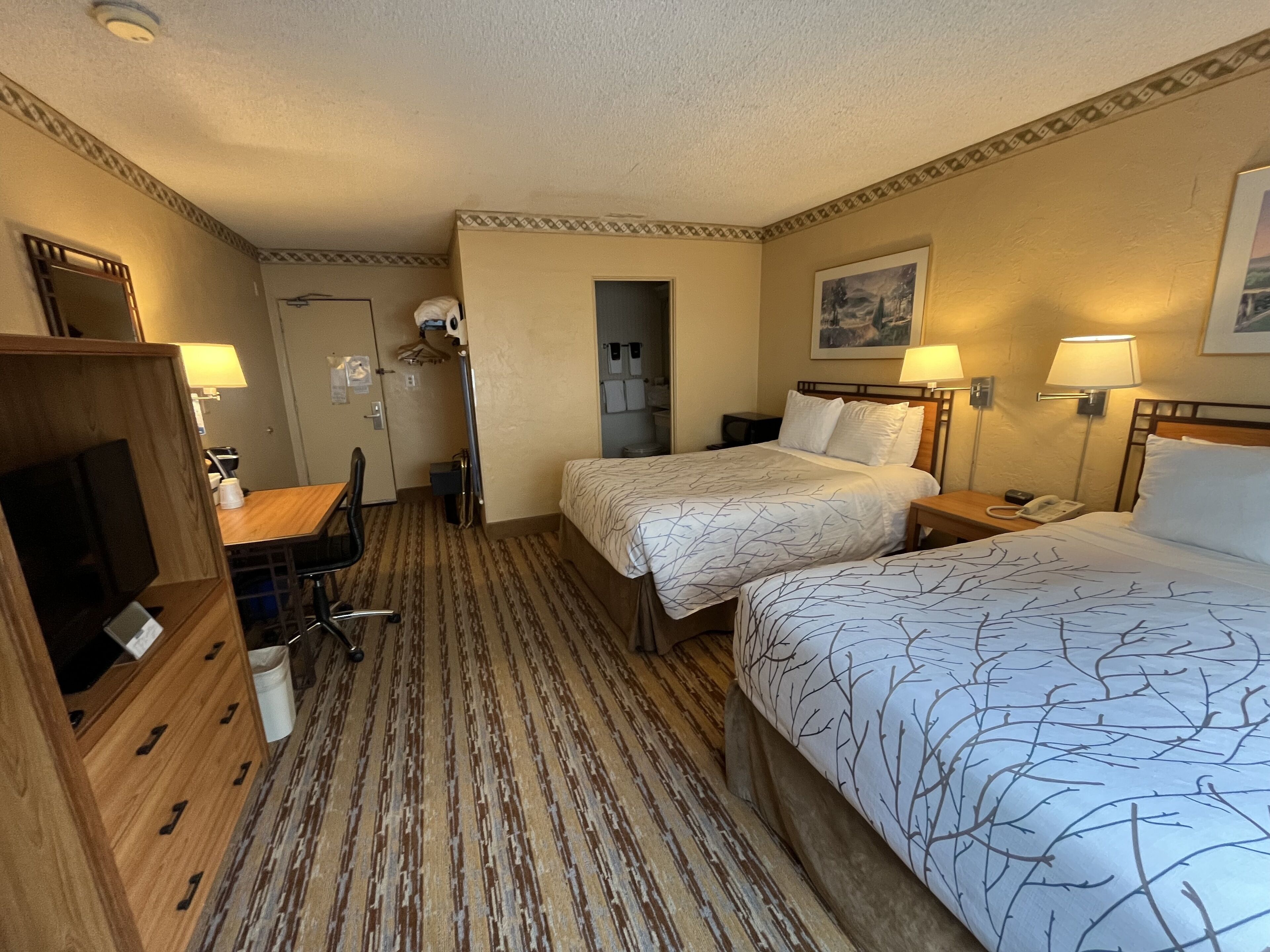 Ett hotellrum med två sängar, ett skrivbord, en stol, en garderob och ett badrum.