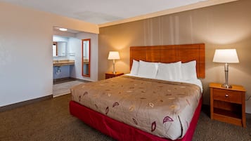 A hotel room with a large bed, two bedside tables with lamps, a wooden headboard, and a bathroom visible through an open door.