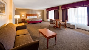 Une chambre d’hôtel comprenant un lit, un canapé, une petite table, deux chaises, un bureau et une fenêtre avec des rideaux.
