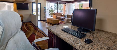 A hotel room with a large desk, a computer, a chair, a sofa, and a television.
