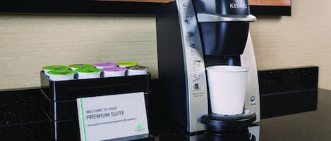 A Keurig coffee maker with a cup holder, a sign for the Premium Suite, and coffee pods on a counter.
