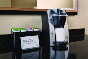 Een Keurig koffiezetapparaat met bekerhouder, een bordje voor de Premium Suite en koffiepads op een aanrecht.