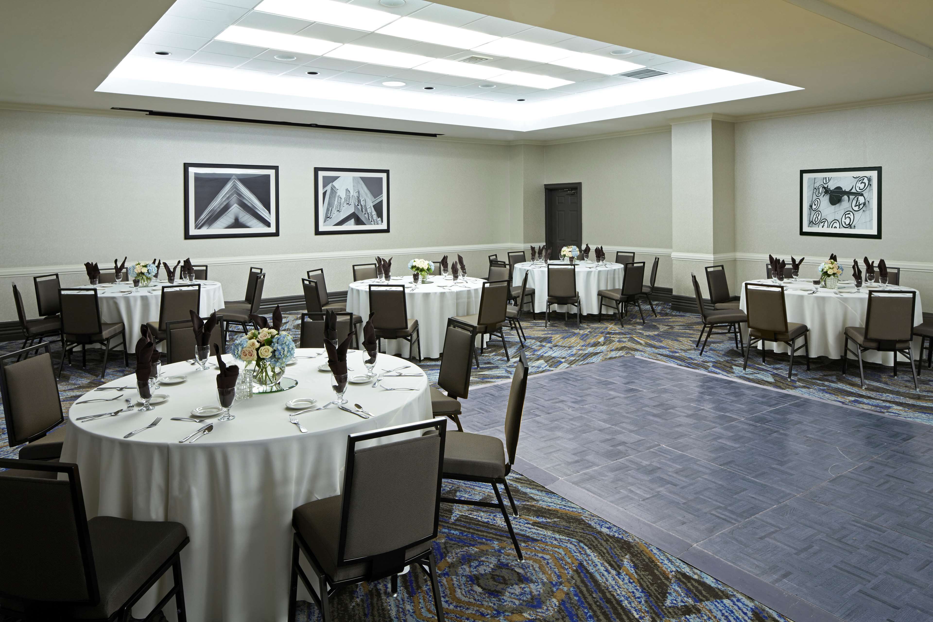Een vergaderzaal met meerdere ronde tafels, elk voorzien van stoelen, witte tafelkleden en decoraties.
