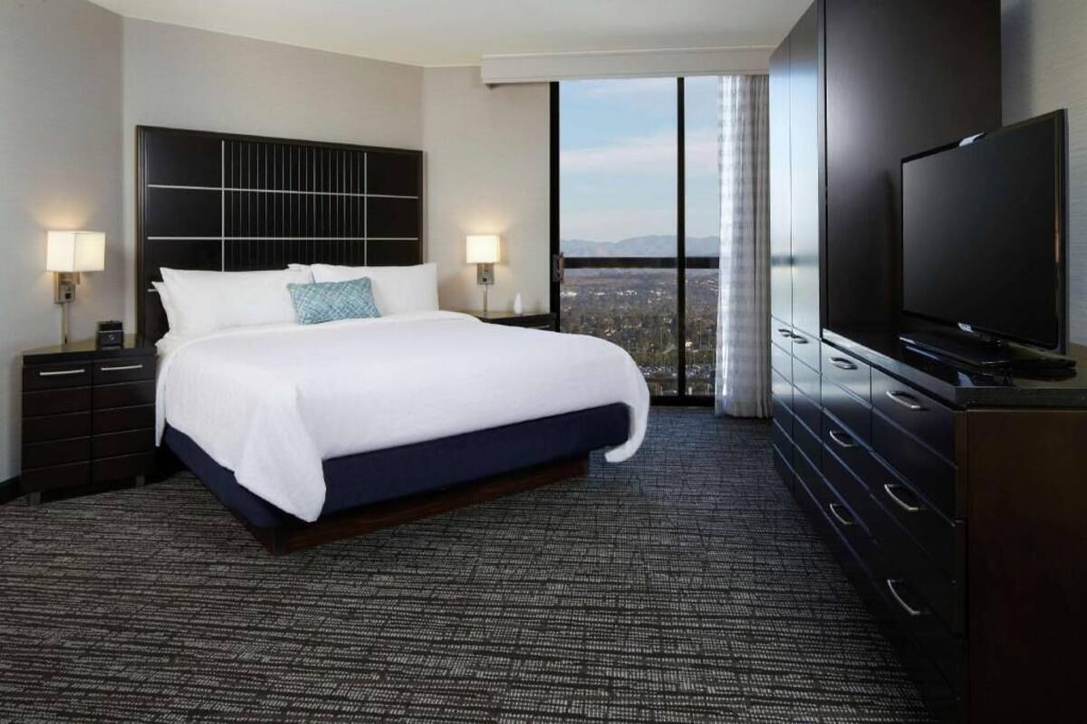 Ein Hotelzimmer mit einem großen Bett, einem Flachbildfernseher, Blick auf die Stadt und modernem Design.