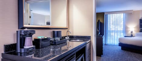 Habitación de hotel con kitchenette, una cama, un espejo grande y vistas al exterior a través de la ventana.