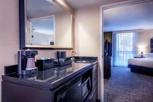 A hotel room with a kitchenette, a bed, a large mirror, and a view of the outside through the window.