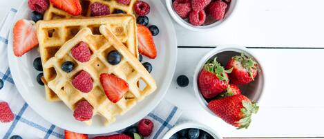 Waffles topped with strawberries and blueberries, accompanied by separate bowls of raspberries and more strawberries.