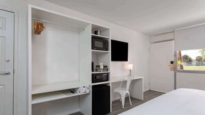 Una camera d'albergo con un letto, una scrivania con una sedia, una TV e un armadio con ripiani.