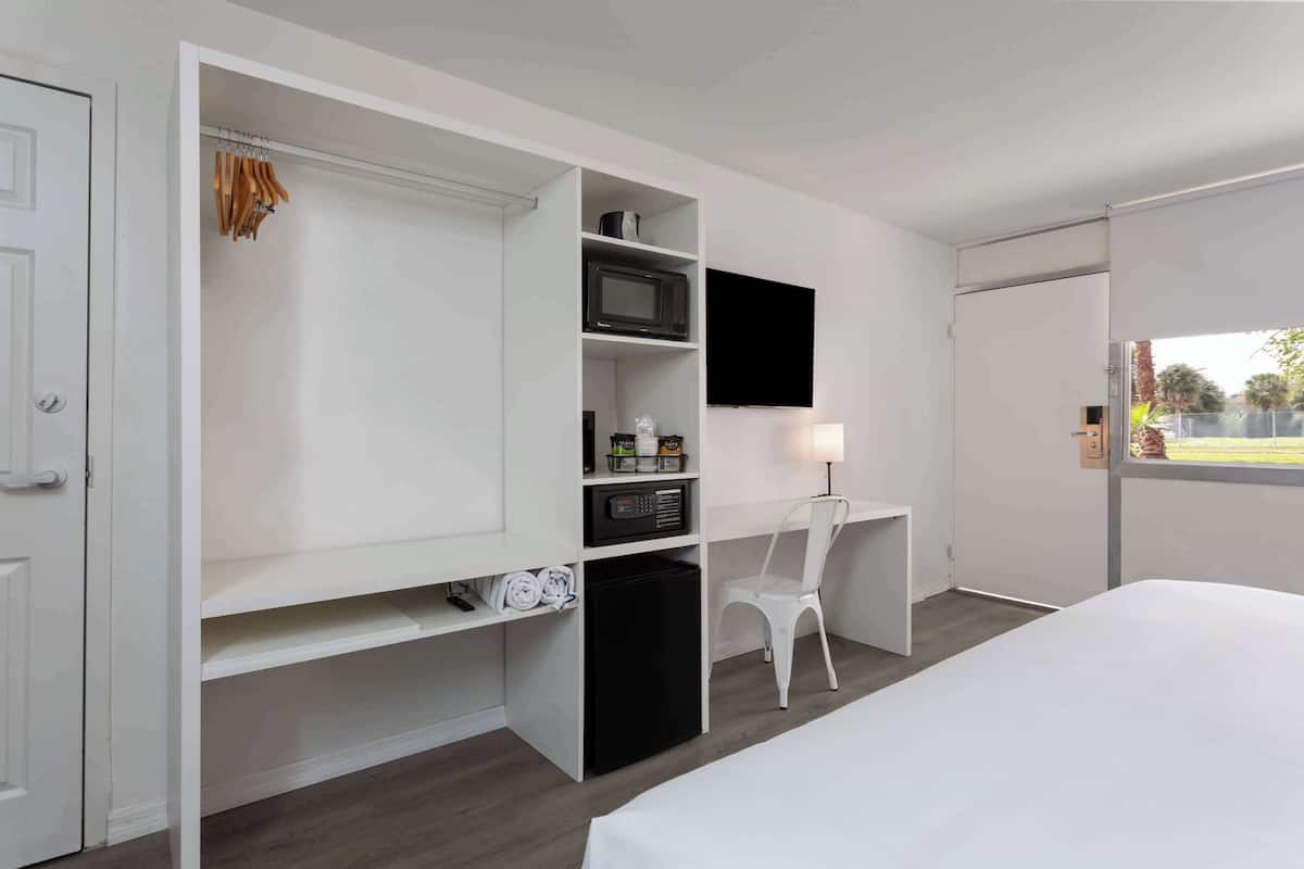 A hotel room with a bed, a desk with a chair, a TV, and a wardrobe with shelves.