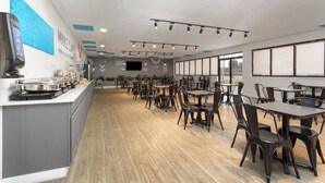 Un'ampia sala da pranzo con numerosi tavoli e sedie, un banco buffet con diverse pietanze e una grande finestra che lascia entrare luce naturale.