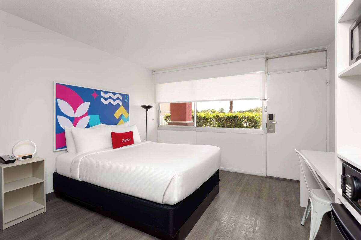 A modern hotel room with a large bed, a desk, and a window with a view of greenery.