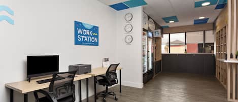A work station area with two desks, chairs, a computer, and a printer. There are clocks on the wall and a sign that reads "Work Station."