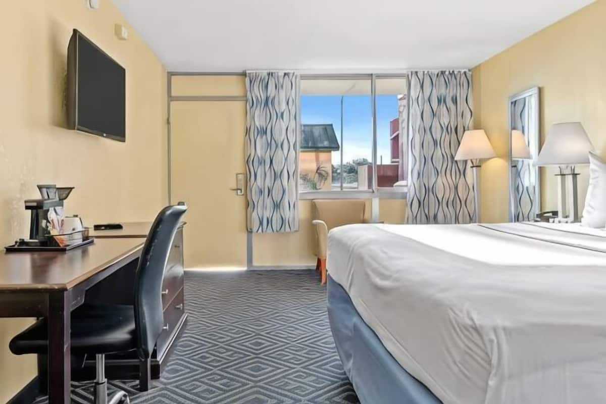 A hotel room with a bed, desk, chair, and a view through a door.