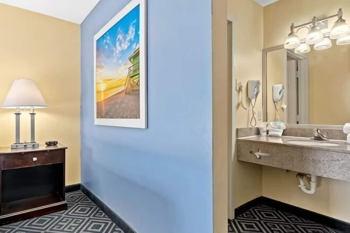 A hotel bathroom with a large mirror, a sink, a hairdryer, and a framed picture on the wall.