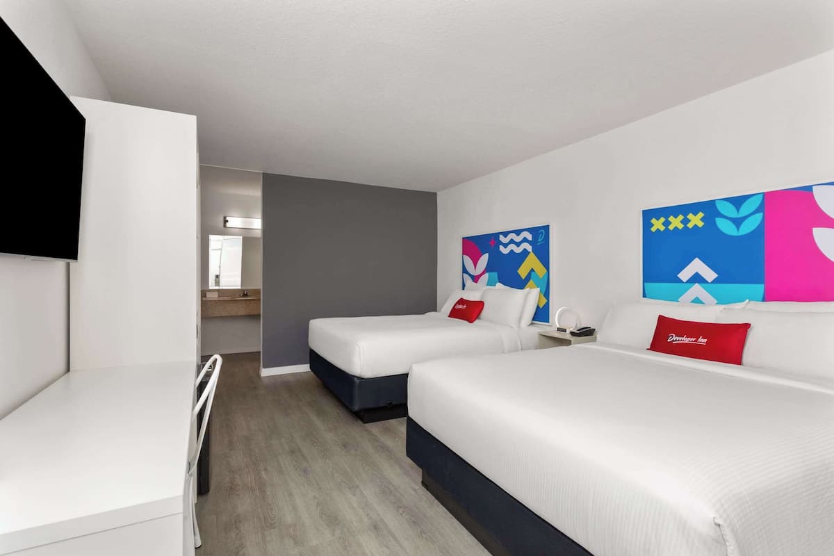 A modern hotel room with two single beds, a small desk, and a TV.