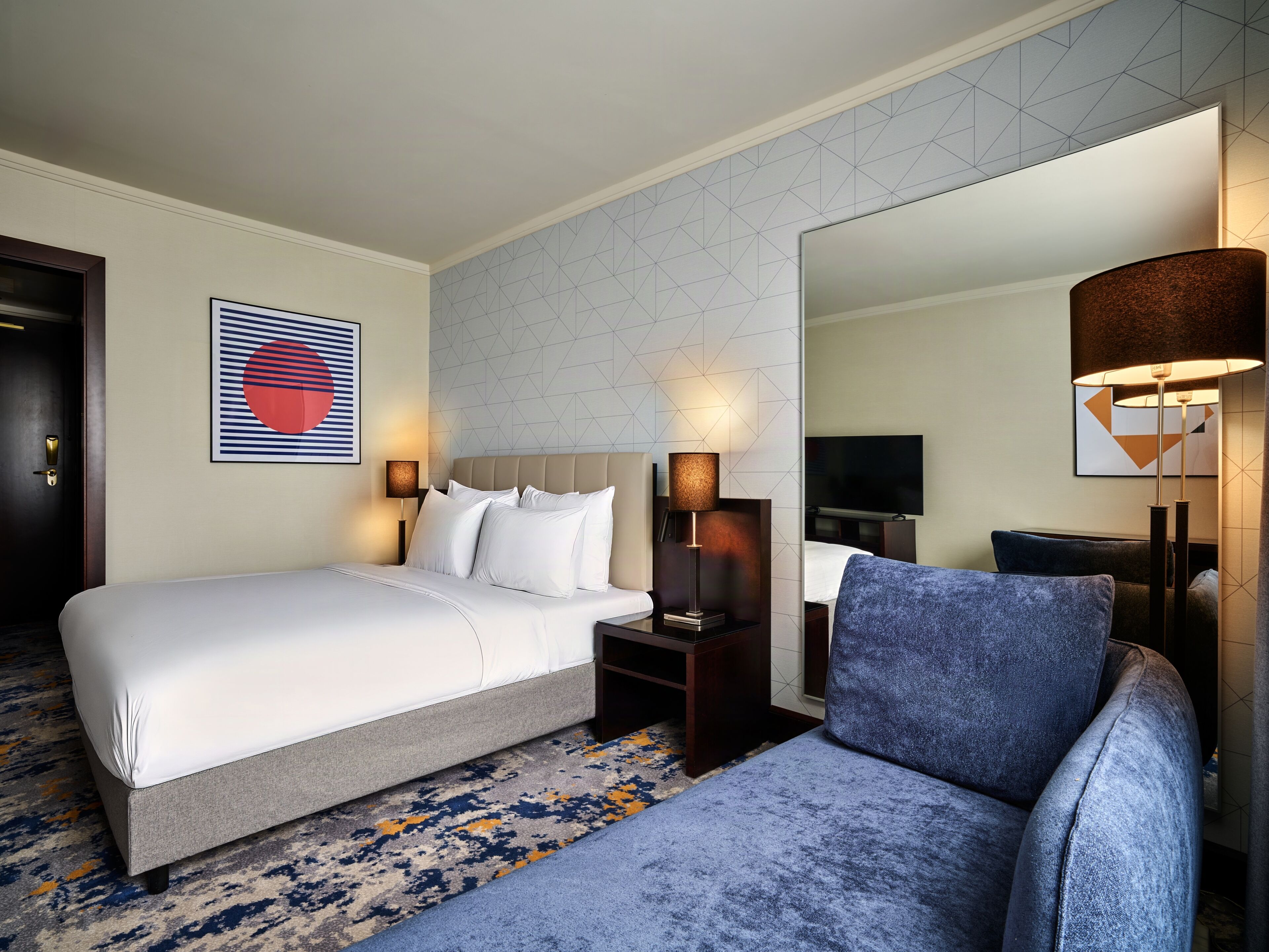Ein Hotelzimmer mit Bett, Sessel, Fernseher und Spiegel.