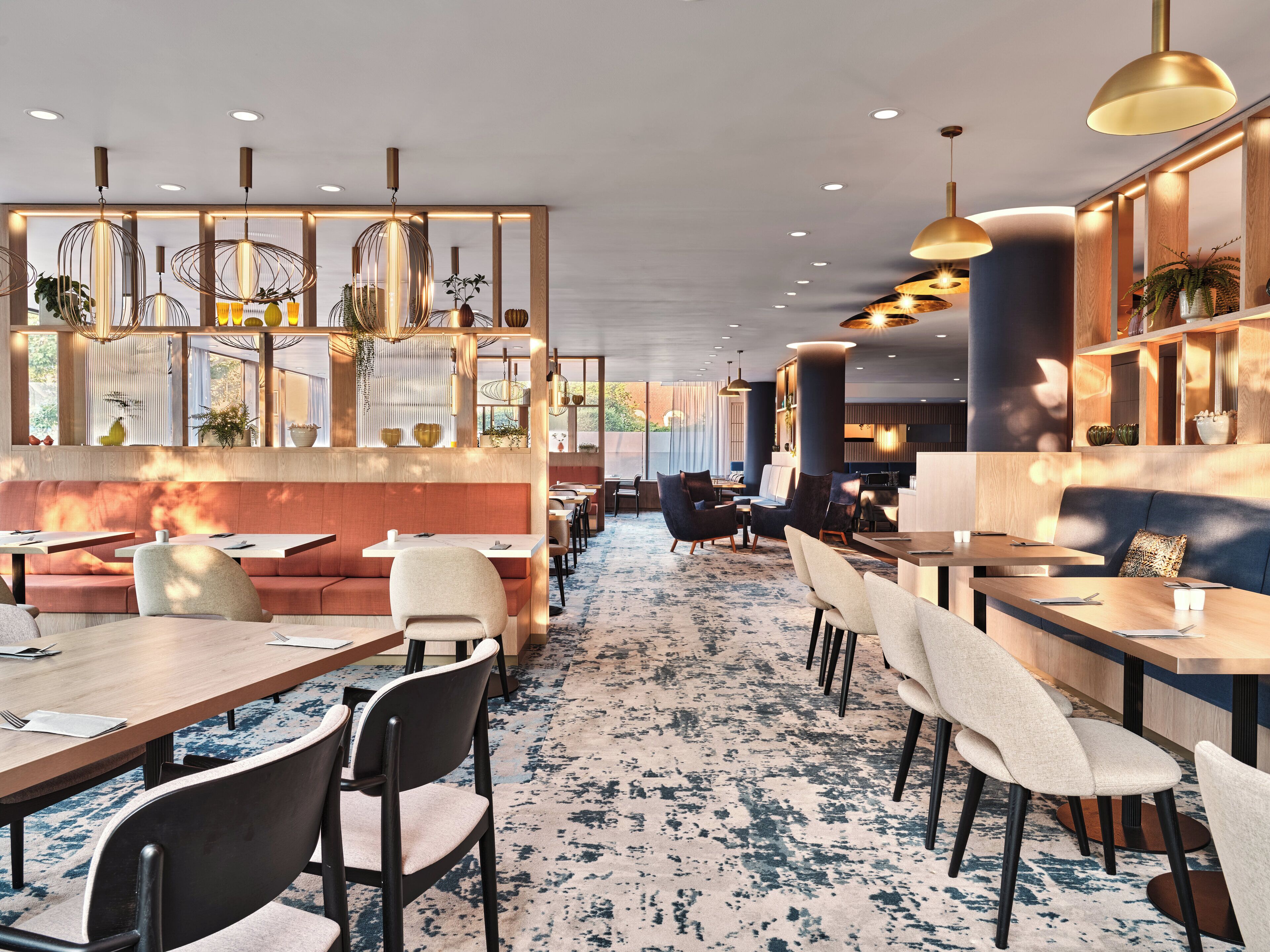 Een modern restaurant met diverse zitmogelijkheden, zoals ruimtes met stoelen en tafels, decoratieve verlichting en een patroonloos tapijt.