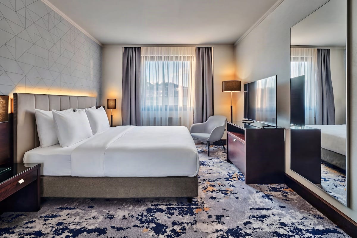 A hotel room with a large bed, a desk, a chair, a TV, and a large mirror.