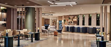 A modern hotel lobby with a reception desk, seating area, and a bar.