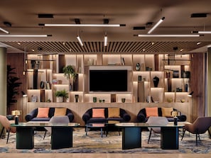 A modern living room with a large flat-screen TV, multiple seating areas, and built-in shelving with decorative items. - Crowne Plaza Bratislava by IHG (Bratislava)