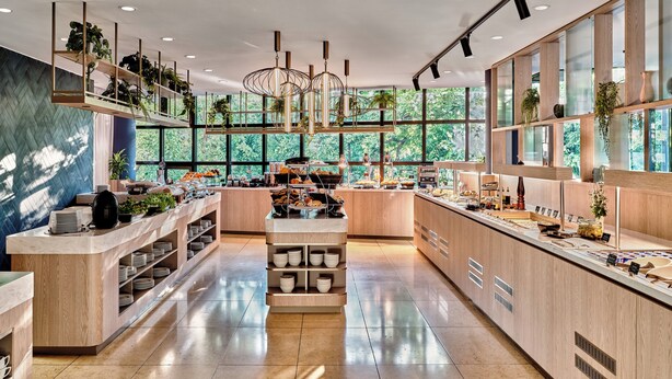 A modern, well-lit kitchen with a central island, ample counter space, and large windows offering a view of greenery outside. - Crowne Plaza Bratislava by IHG (Bratislava)