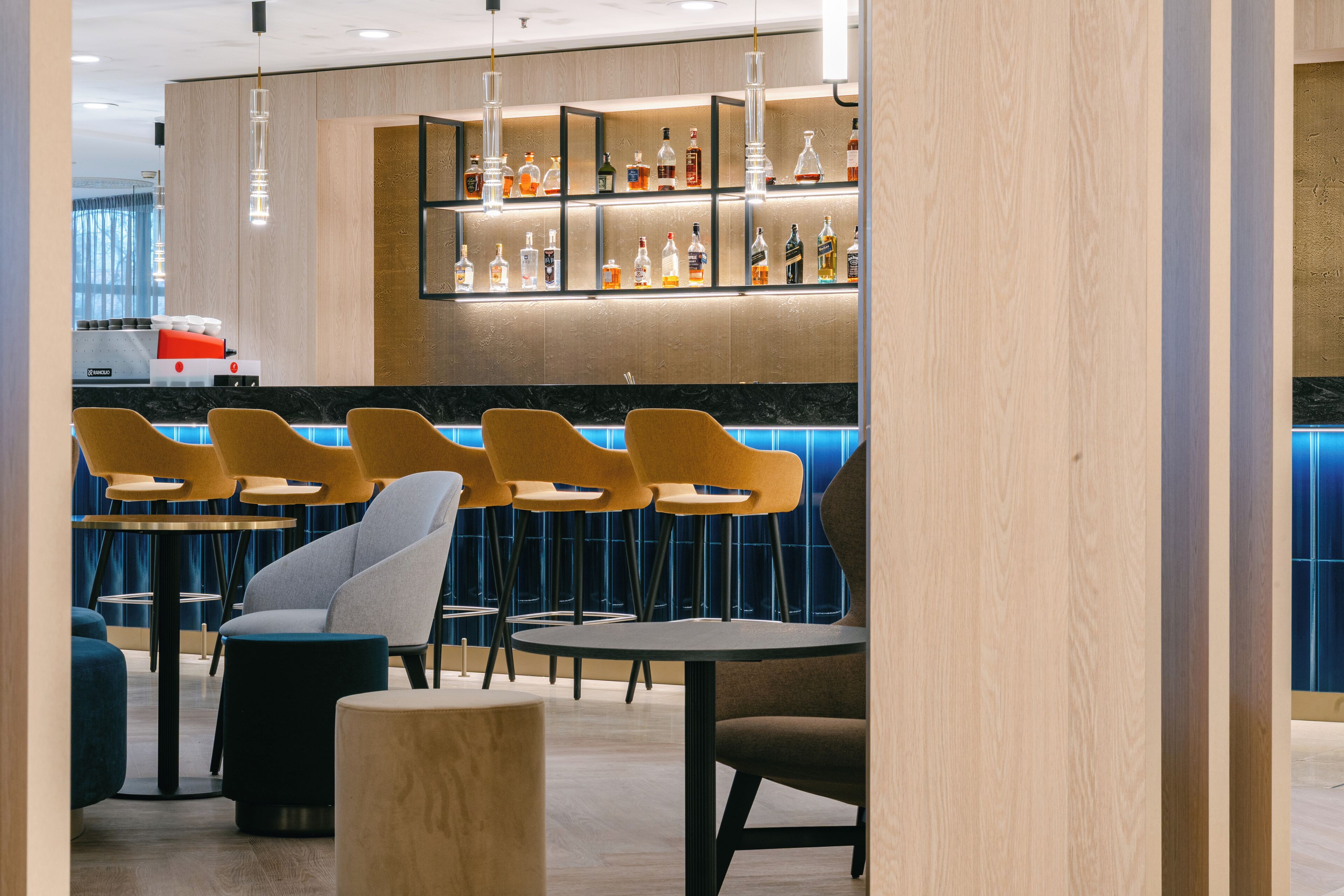Zona bar con scaffali in legno che espongono bottiglie, sedie gialle e un bancone.