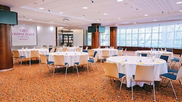 A conference room at Crowne Plaza with round tables, chairs, and a large screen displaying the hotel's name.