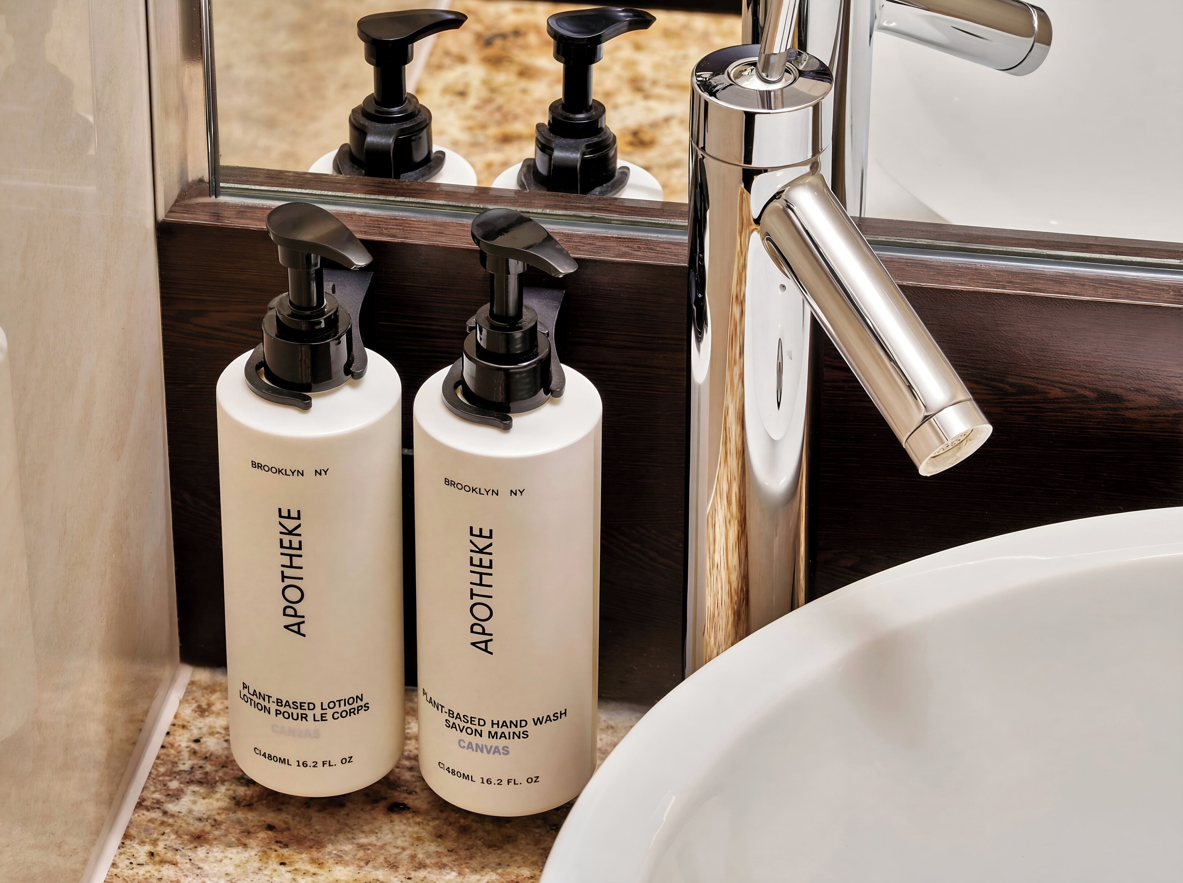 Un baño con un lavamanos, dos botellas de loción Apothéke a base de plantas, y un espejo que refleja un grifo.