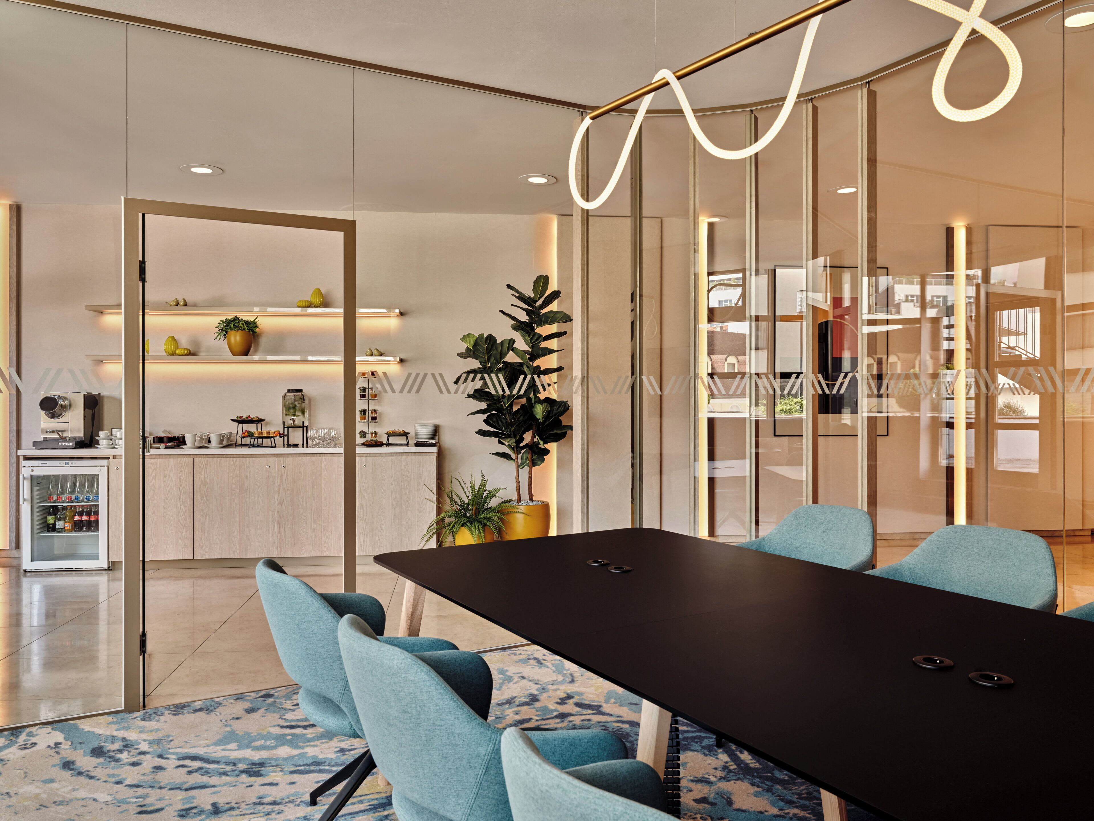 A modern meeting room with a black table, teal chairs, and a glass partition.