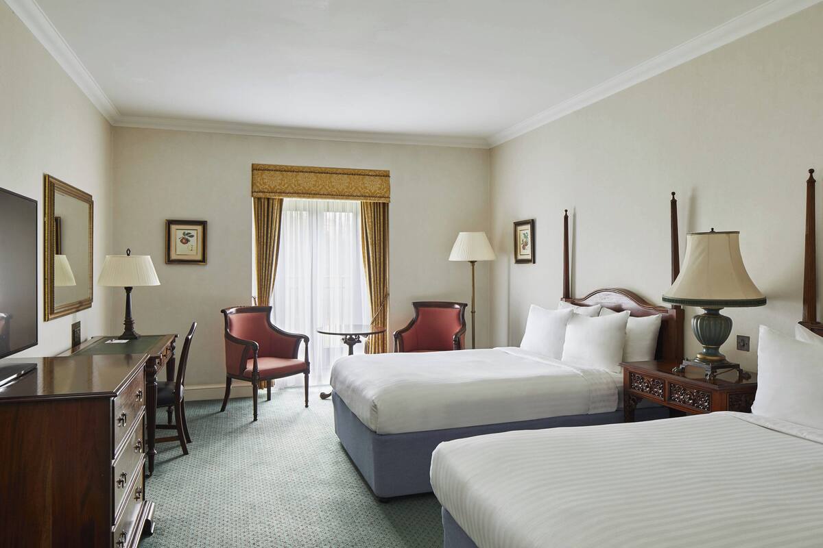 A hotel room with two beds, a desk with a chair, a TV, and two lamps.