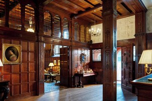 A grand room with wooden paneling, a chandelier, and a large window with a view.