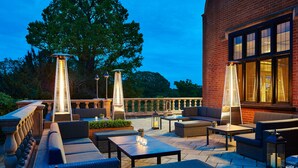 An outdoor patio area with seating arrangements, tables, and decorative lighting. - Hanbury Manor Marriott Hotel & Country Club (Ware)
